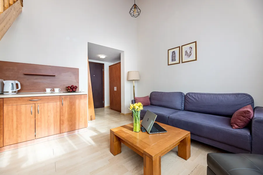 Svetainė su mėlyna sofa, virtuvėle ir laiptais