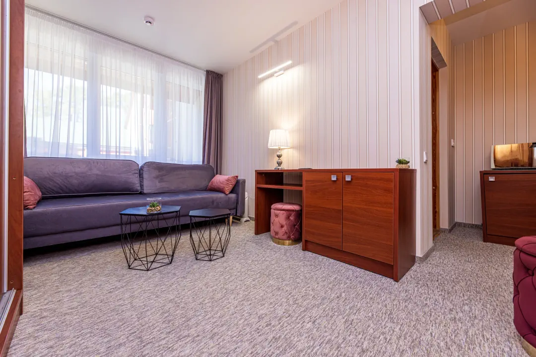Svetainė su pilka sofa, dviem kavos staliukais ir medine komoda